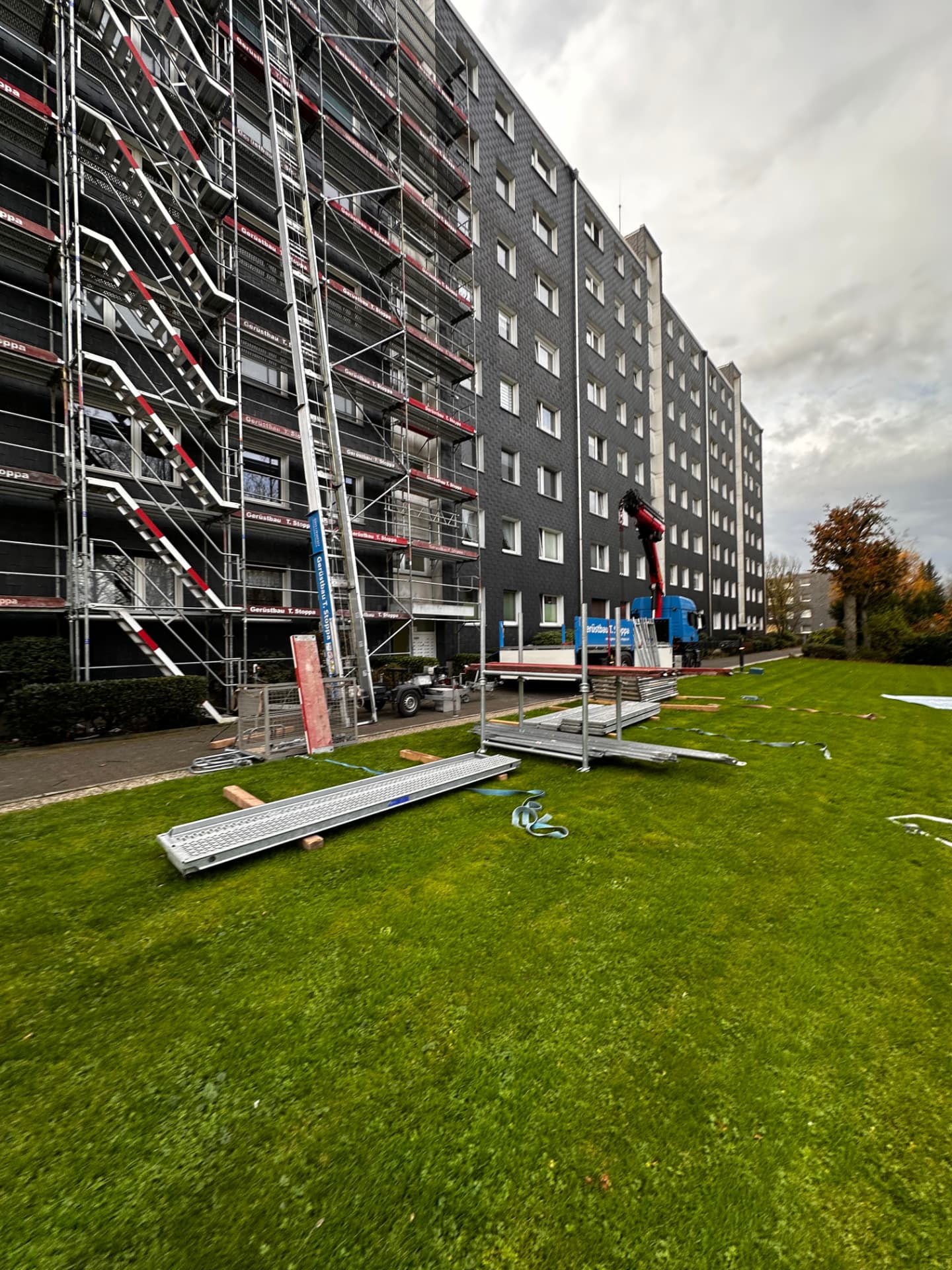 Mobiler Bauaufzug an einem voll eingegrüsteten Wohnhochhaus von Gerüstbau Stoppa, Material liegt bereit, Stoppa-Lkw mit Ladekran davor