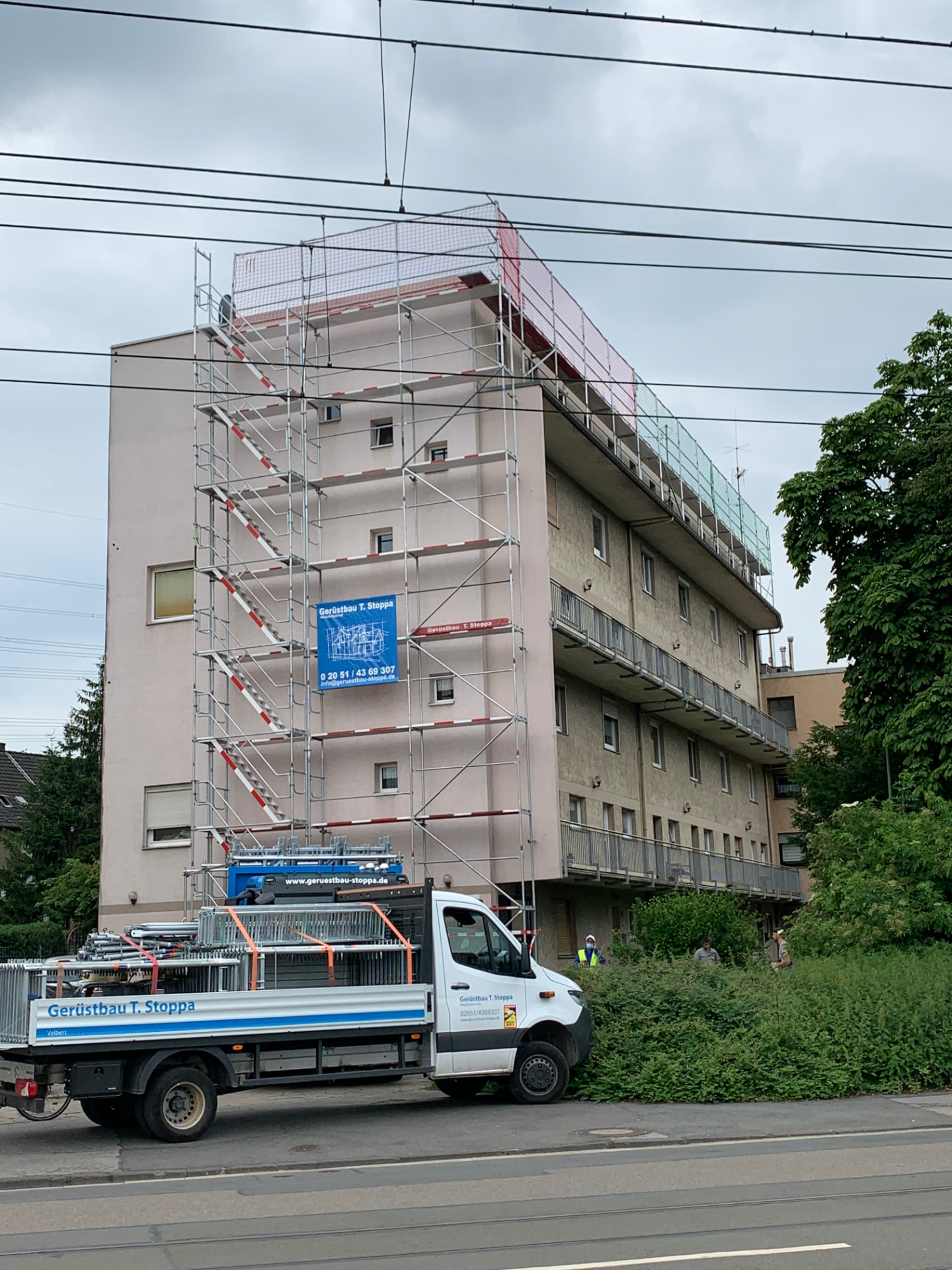 Mehrfamilienhaus in Essen mit Dachdeckergerüst und Treppenturm von Gerüstbau Stoppa zur Flachdachsanierung, weißer Stoppa-Lkw mit Gerüstmaterial davor