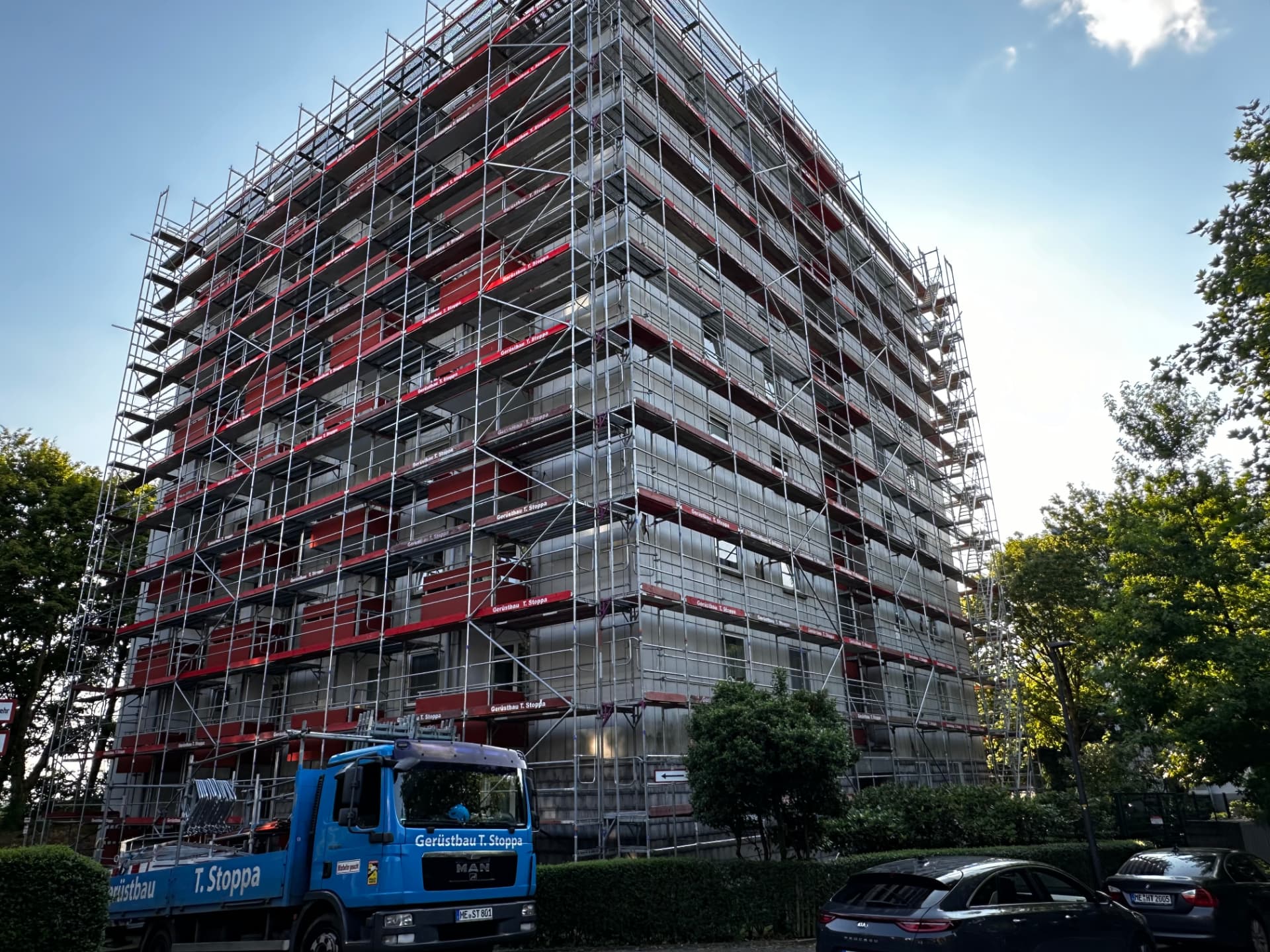 Wohnhochhaus in Heiligenhaus mit vollflächigem Fassadengerüst von Gerüstbau Stoppa, rote Gerüstbretter, blauer Stoppa-Lkw davor