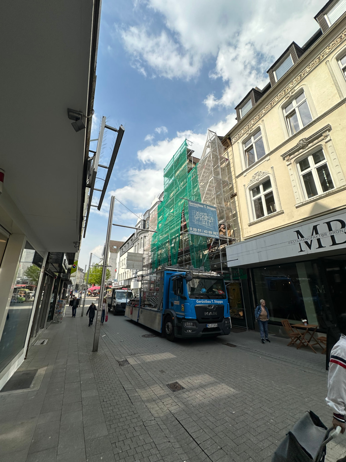 Fassadengerüst mit grünen Staubschutznetzen an einem Wohn- und Geschäftshaus in der Velberter Innenstadt, blauer Stoppa-Lkw in der Fußgängerzone
