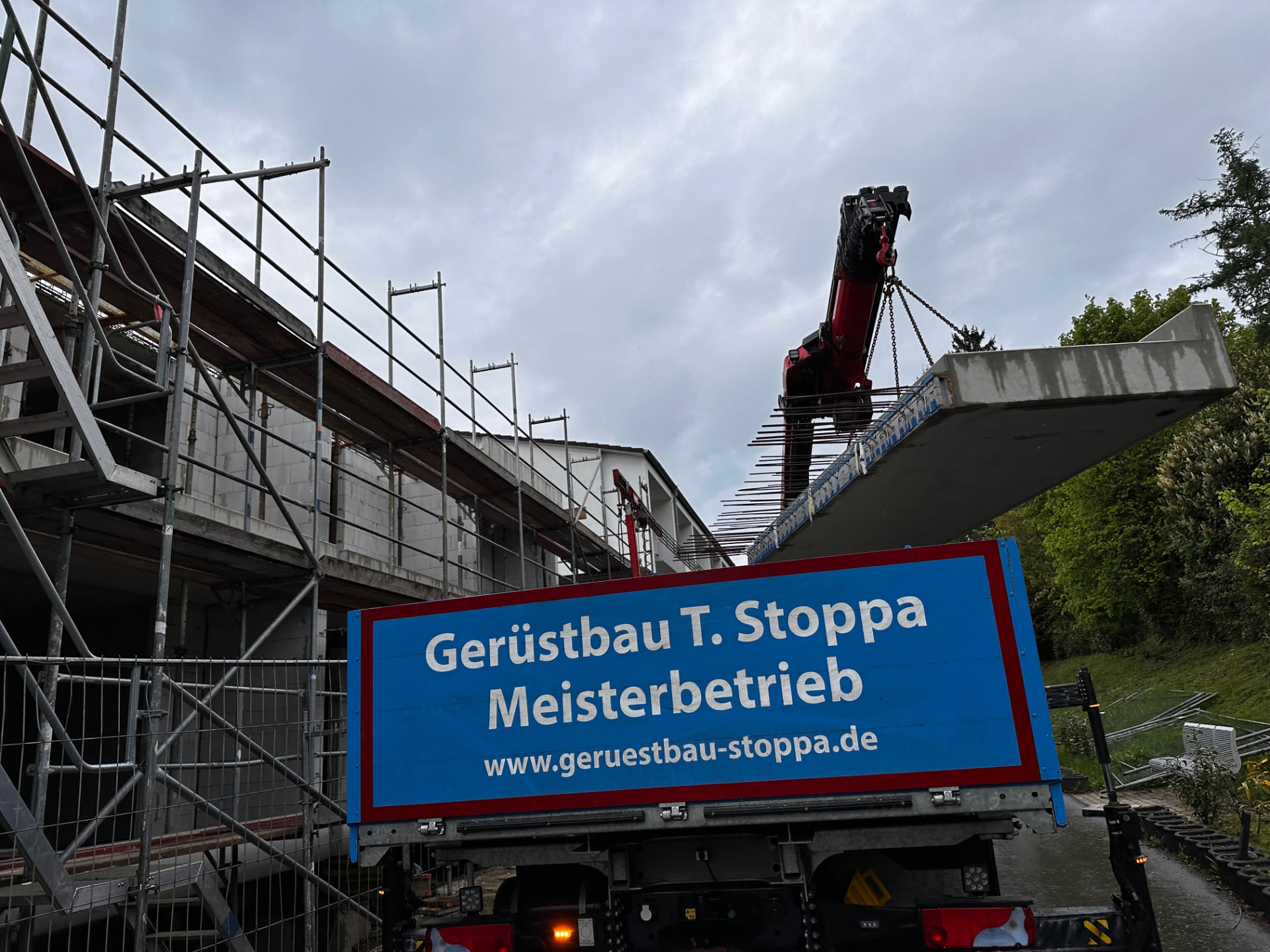 Roter Stoppa-Ladekran hebt eine schwere Betonplatte über eine eingerüstete Baustelle