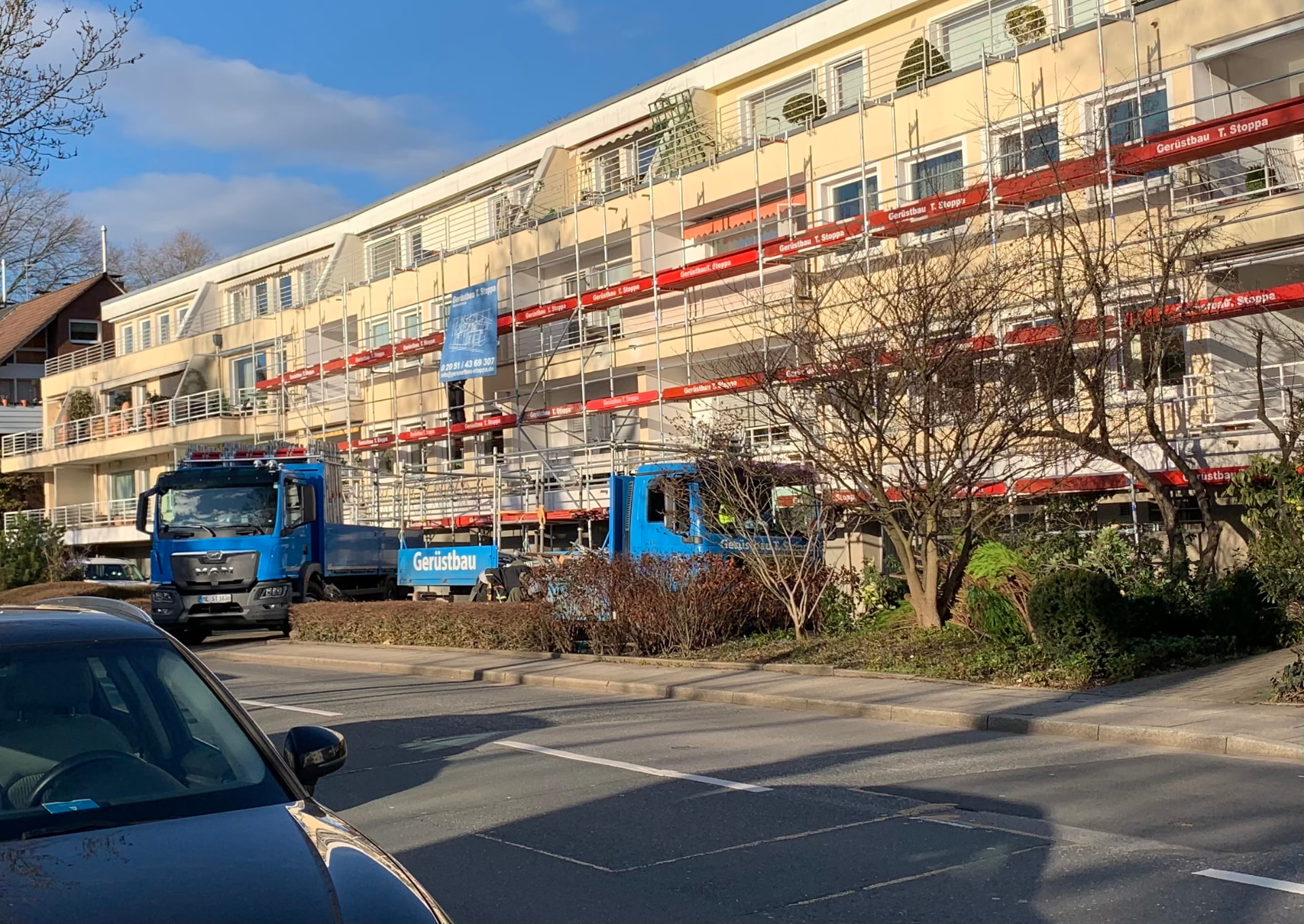 Langgezogene Wohnanlage in Essen Werden mit vollflächigem Fassadengerüst von Gerüstbau Stoppa, rote Stoppa-Bretter und blaue Stoppa-Lkw davor