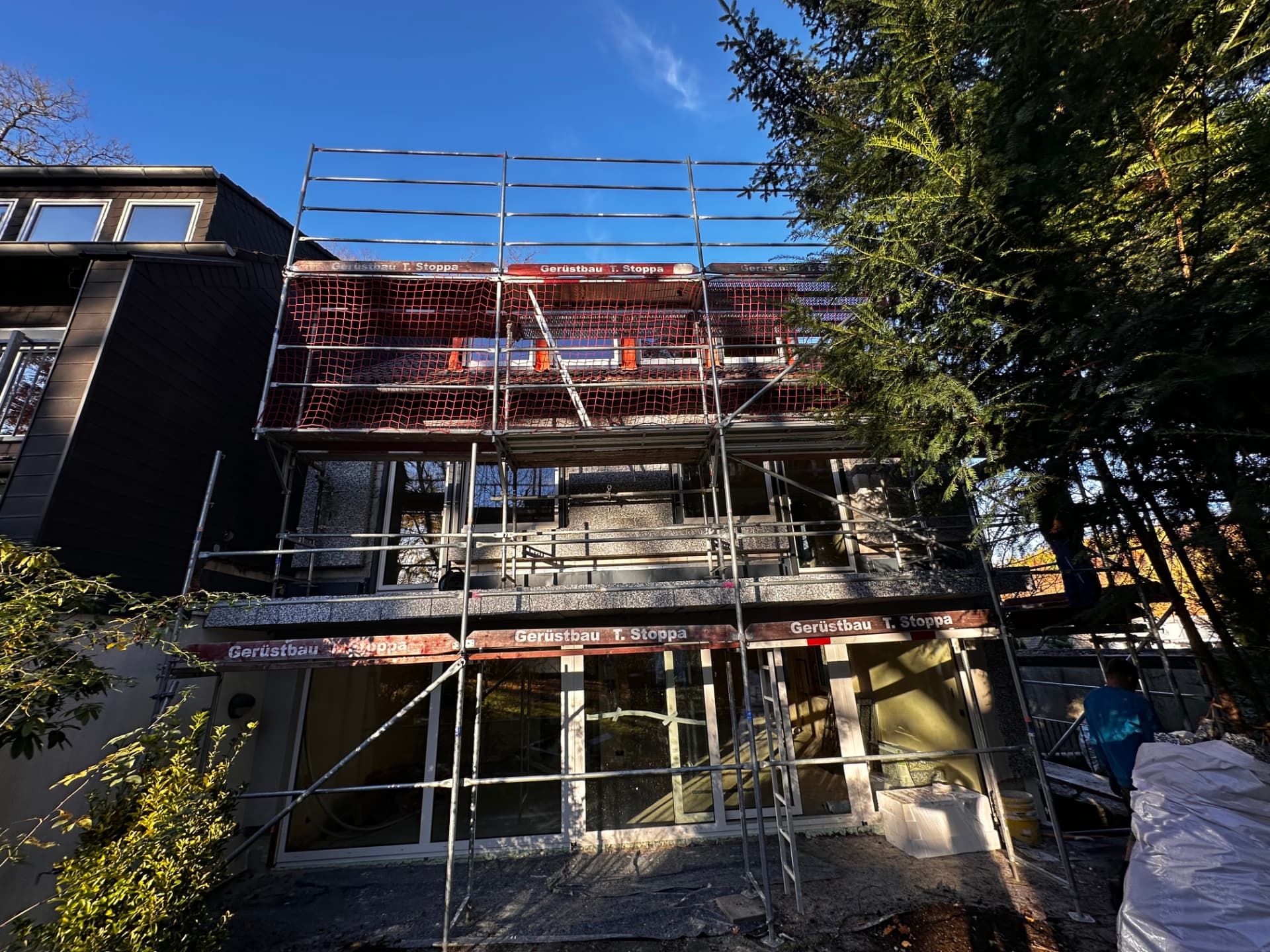 Wohnhaus in Velbert mit Fassadengerüst von Gerüstbau Stoppa, rote Stoppa-Bretter und rotes Fangnetz für Fassaden- und Dacharbeiten